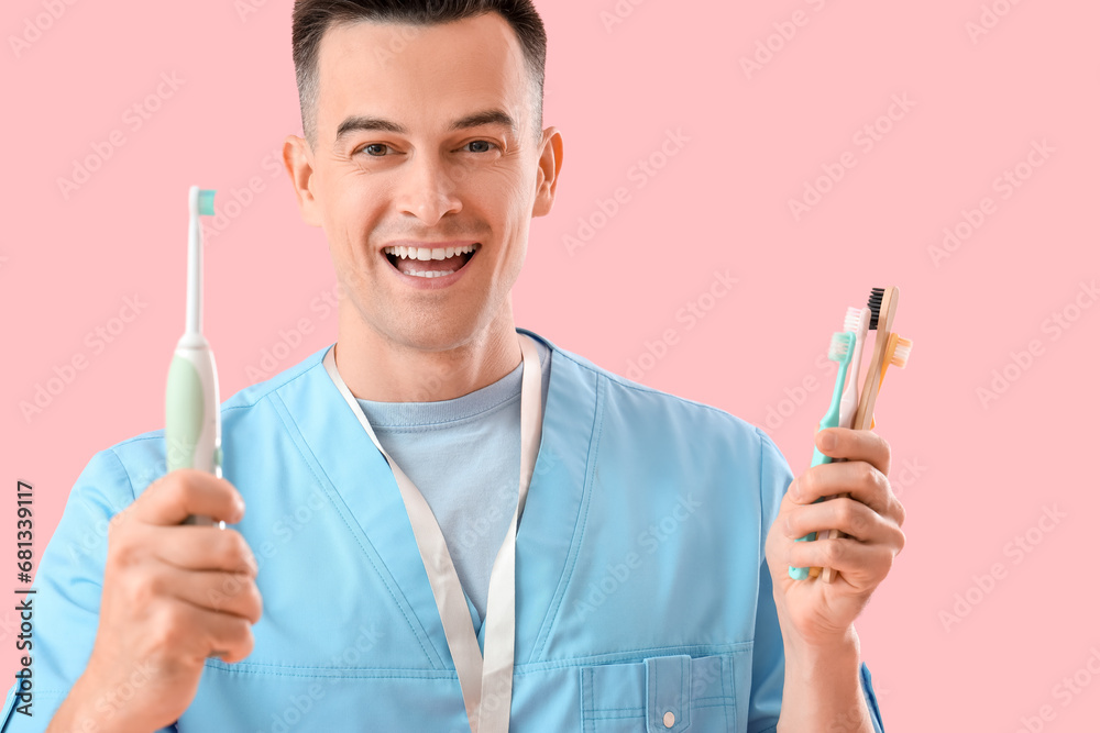 Male dentist with toothbrushes on pink background, closeup