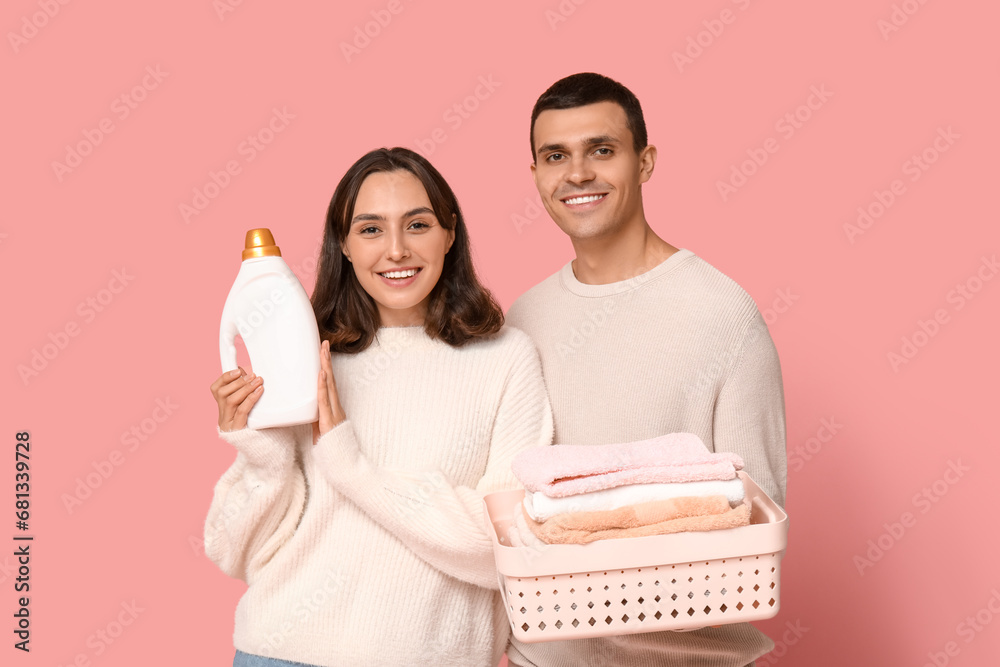 Young couple with laundry basket and bottle of detergent on pink background