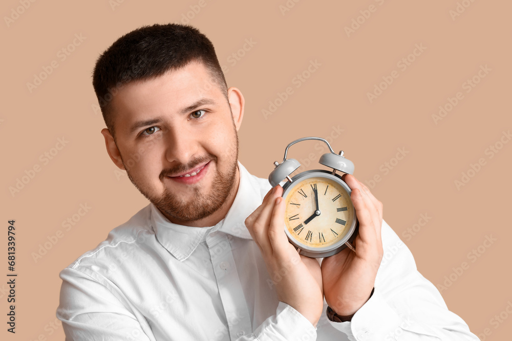 Young happy businessman with alarm clock on beige background. Time management concept