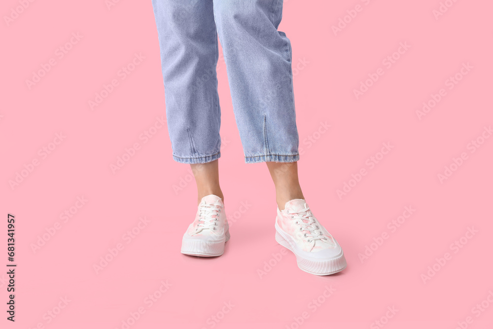 Legs of young woman in stylish white sneakers on pink background