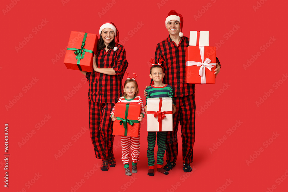 Happy family in pajamas with Christmas gifts on red background