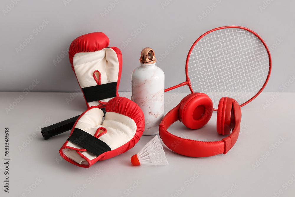 Badminton racket with shuttlecock, boxing gloves, headphones and sports bottle on grey background