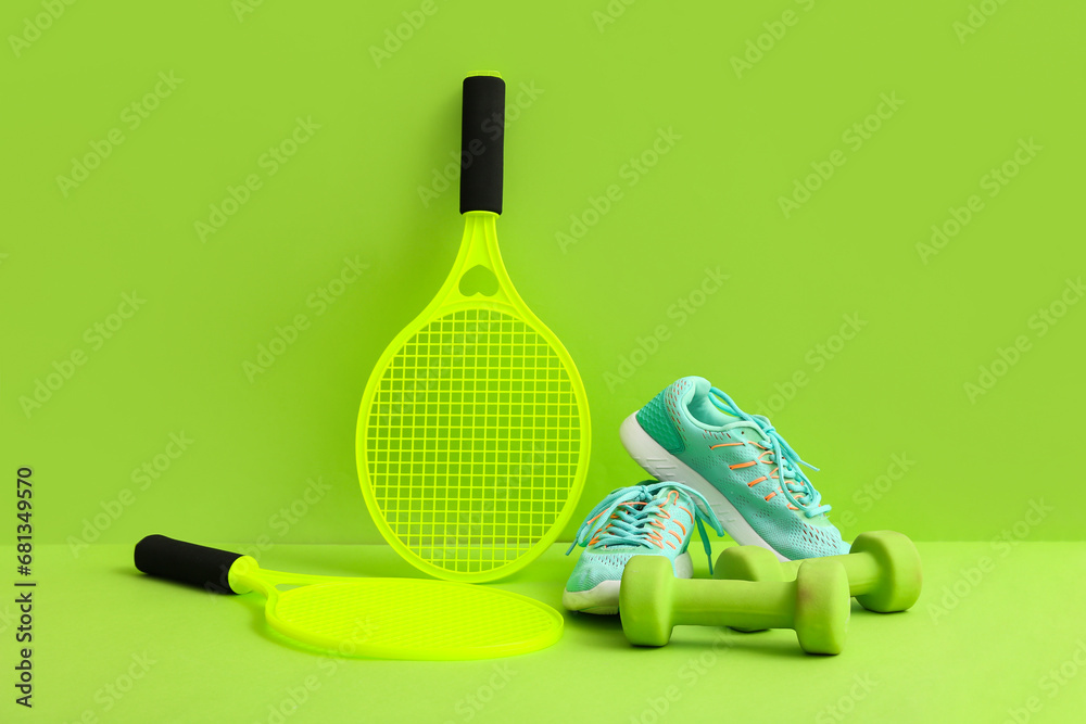 Tennis rackets with dumbbells and sneakers on green background