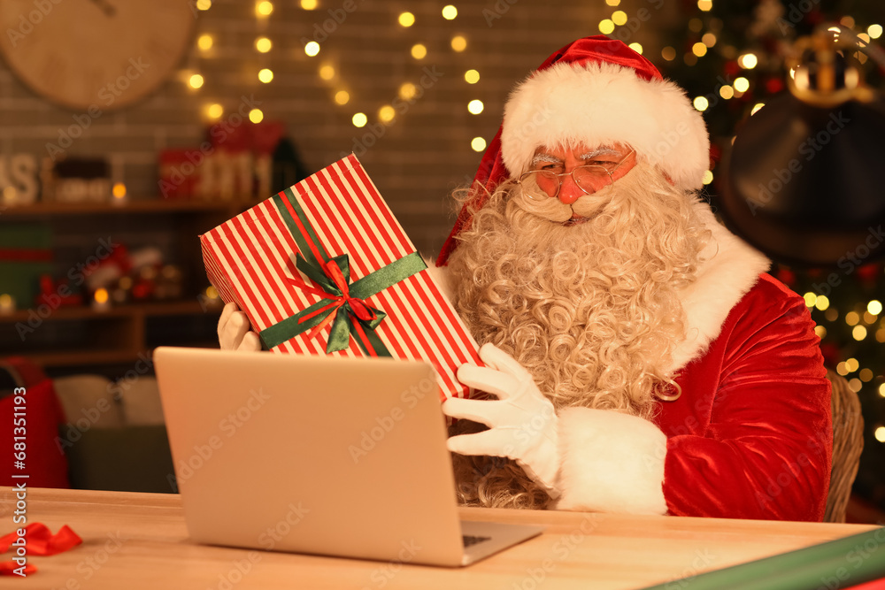 Santa Claus with laptop and Christmas gift at home