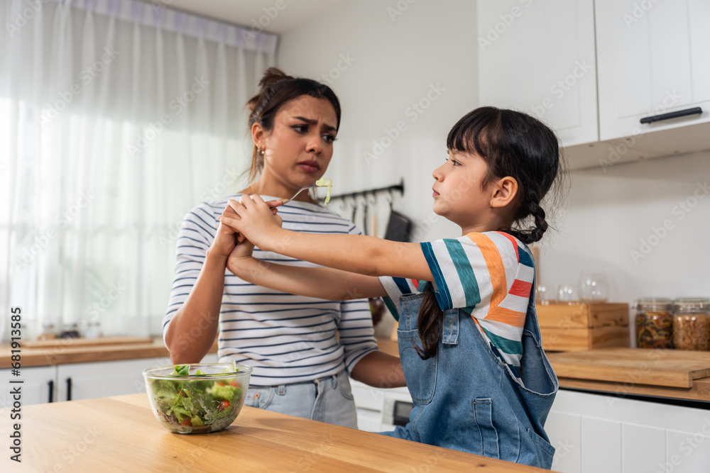 Caucasian mother teach and motivate young daughter eat green vegetable. 