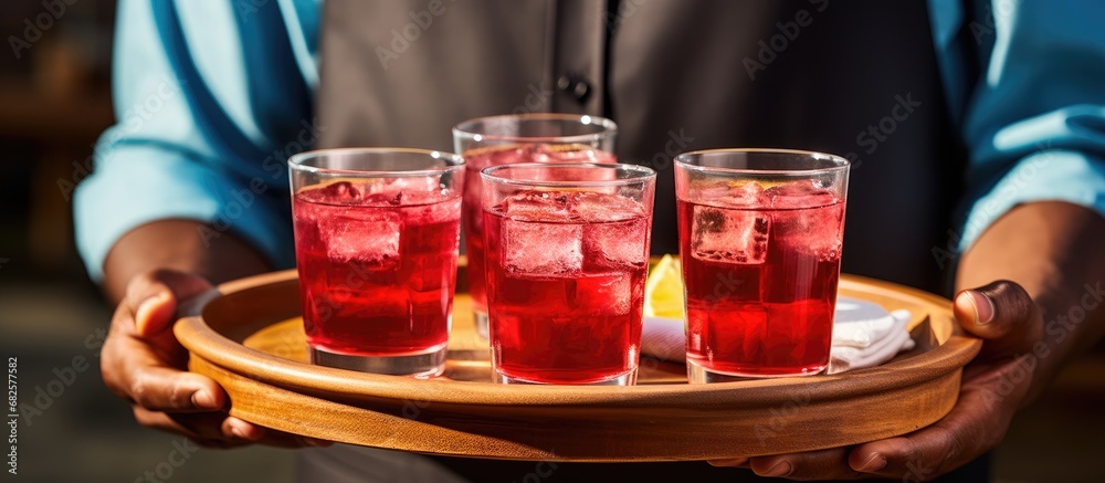 In the warm summer breeze, a wooden tray adorning glasses filled with vibrant cranberry juice is carried by a manufacturing worker, accompanied by a cup and saucer, bringing a refreshing beverage with